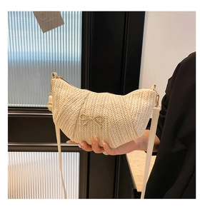 Detailed view of beige woven crescent bag with gold bow ornament and leather strap