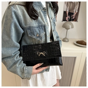 Detail of black faux leather clutch with stone pattern and gold bow-knot hardware decoration