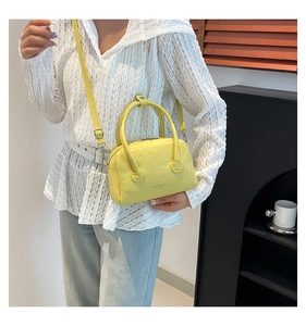 Sac bowling jaune en cuir grainé avec poignées et bandoulière porté par un mannequin