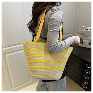 Side view of large woven straw tote bag with yellow stripes and fabric shoulder strap