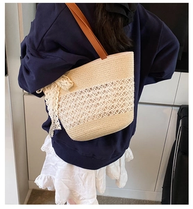 Straw woven shoulder bag with white lace bow detail shown on a model in a casual setting