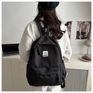 Rear view of a black minimalist backpack with a smile patch worn by a person at a desk