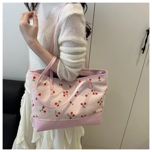 Detail of pink canvas tote bag with cherry print worn over the shoulder by a model