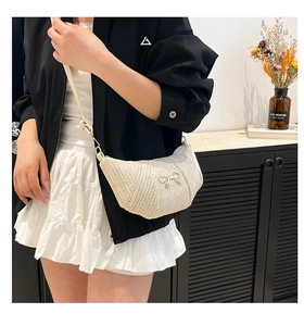 Detail of cream woven crescent bag featuring a delicate metal bow and fine straw texture