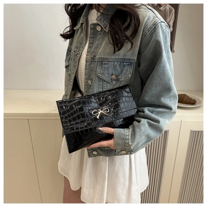 Detail of black faux crocodile patent leather clutch with a gold bow metal buckle clasp