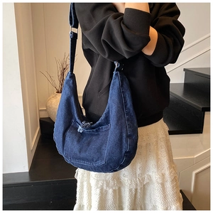 Detail of dark blue denim crescent bag showing frayed edge pocket and wide shoulder strap