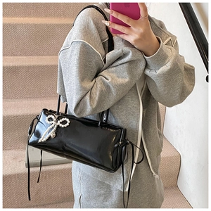 Close-up of black patent leather underarm bag with a pearl bow charm on shoulder