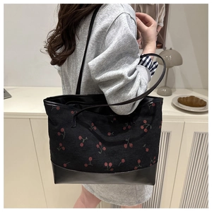Detail of black corduroy tote bag with cherry print and leather bottom on model