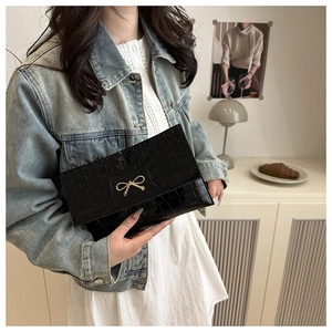 Close-up of black crocodile pattern PU leather handbag with golden bow metal buckle