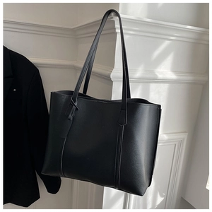 Detail of a black leather tote bag with vertical stitching hanging against a white wall