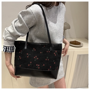 Détail d'un sac cabas noir avec motif cerise porté par un mannequin en intérieur