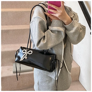 Glossy black underarm bag with pearl bow pendant detail shown in a lifestyle scene