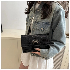 Detail of black faux leather clutch with crocodile texture and gold bow buckle