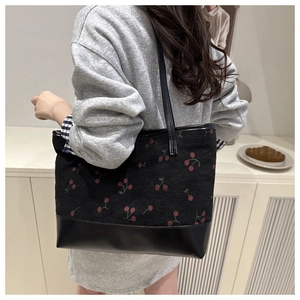 Close-up of black corduroy tote bag featuring red cherry print and long shoulder strap