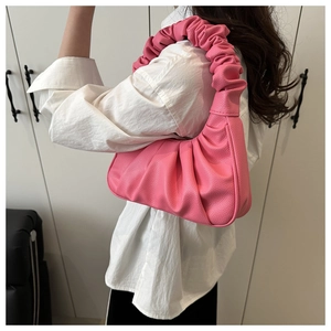 Elegante borsa a tracolla rosa plissettata mostrata in dettaglio su una persona in camicia bianca.