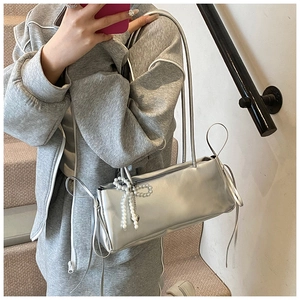Detail of silver metallic pillow bag with pearl bow charm worn on the shoulder