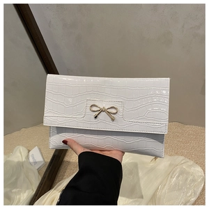 Detailed close-up of white crocodile texture PU leather clutch with golden bow decoration