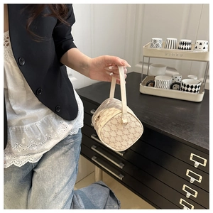 Detail of a creamy white cylindrical Boston bag with M-letter pattern held by a model