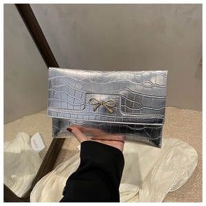 Macro shot of silver crocodile pattern PU leather clutch bag with golden bow hardware