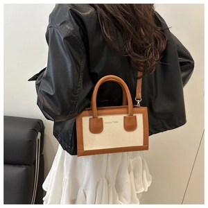 Detail of a beige canvas and brown leather tote bag styled with a black leather jacket