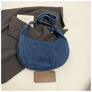 Detail view of a large denim crescent bag with frayed edges and adjustable strap
