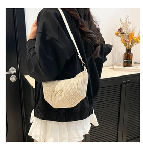 Detail of beige straw croissant bag with metallic bow buckle and adjustable strap