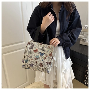 Detailed view of cream tote bag featuring colorful butterfly embroidery and black straps