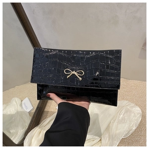 Detail of glossy black crocodile pattern PU leather clutch with golden bow buckle