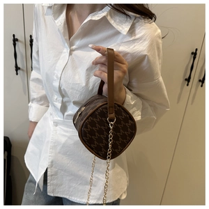 Detail of a brown cylindrical bag with M-pattern print and gold chain strap handle