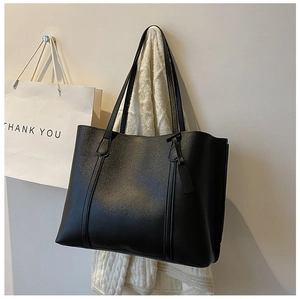 Detail of large black matte leather tote bag featuring vertical stitching and tag
