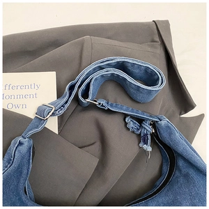 Detailed macro of denim crescent bag showing adjustable strap and silver metal buckle