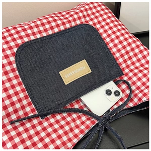 Macro view of red and white plaid tote bag featuring a denim pocket with a leather patch