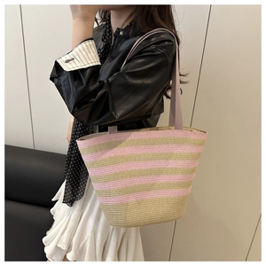 Detail of pink and beige striped straw tote bag with lavender handles on shoulder