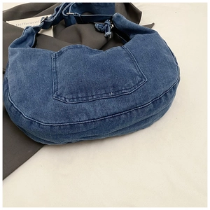 Close-up of a blue denim crescent bag featuring a practical front pocket with topstitching
