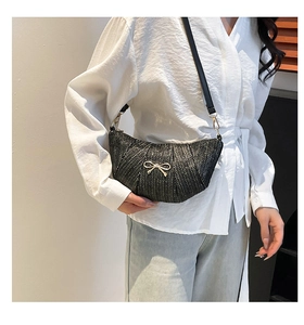 Detail of black woven crescent bag featuring a delicate gold bow and textured V-pattern