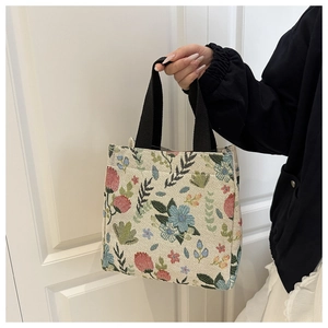 Detailed view of floral embroidery on a beige canvas tote bag with black strap handles