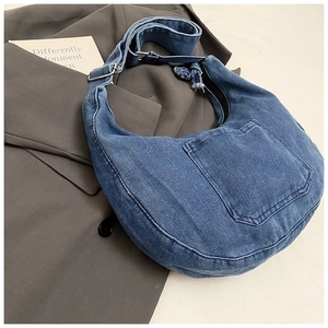 Detail of blue denim crescent bag showing front pocket and adjustable wide shoulder strap