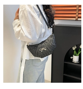 Detail of black woven crossbody bag with gold bow accent worn by a model