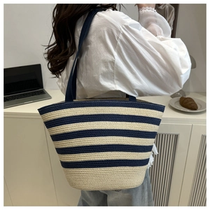 Detail of blue and beige striped straw tote bag worn by a model in a casual indoor setting