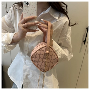 Pink crossbody bag with M-pattern print and gold chain strap held by a model