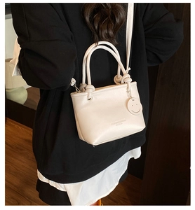 Chic beige bucket bag with knot handle and smiley charm shown on model in modern setting