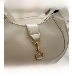 Détail du sac hobo en cuir crème avec coutures incurvées et fermoir crochet en métal doré