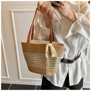 Close-up of woven straw tote bag with brown leather handles and white lace bow detail
