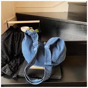 Detail of dark blue denim hobo bag with adjustable strap and metal buckle on books