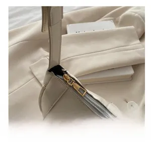 Détail d'une fermeture éclair dorée lisse sur un sac sous le bras de couleur crème
