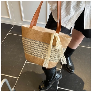 Detail of woven straw tote bag with brown leather handles and decorative white lace scarf