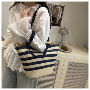 Detail of navy and beige striped straw tote bag carried in a French lifestyle setting