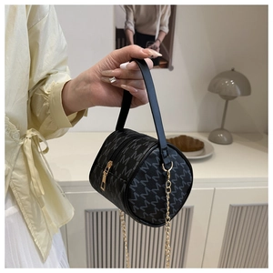 Close-up of black cylinder handbag with grey monogram print and gold chain strap