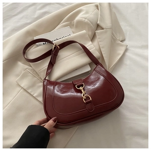 Détail macro du sac selle en cuir verni bordeaux avec crochet en métal doré