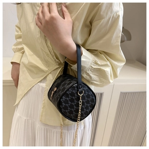 Detail of black cylindrical handbag featuring gray M-letter print and gold chain strap